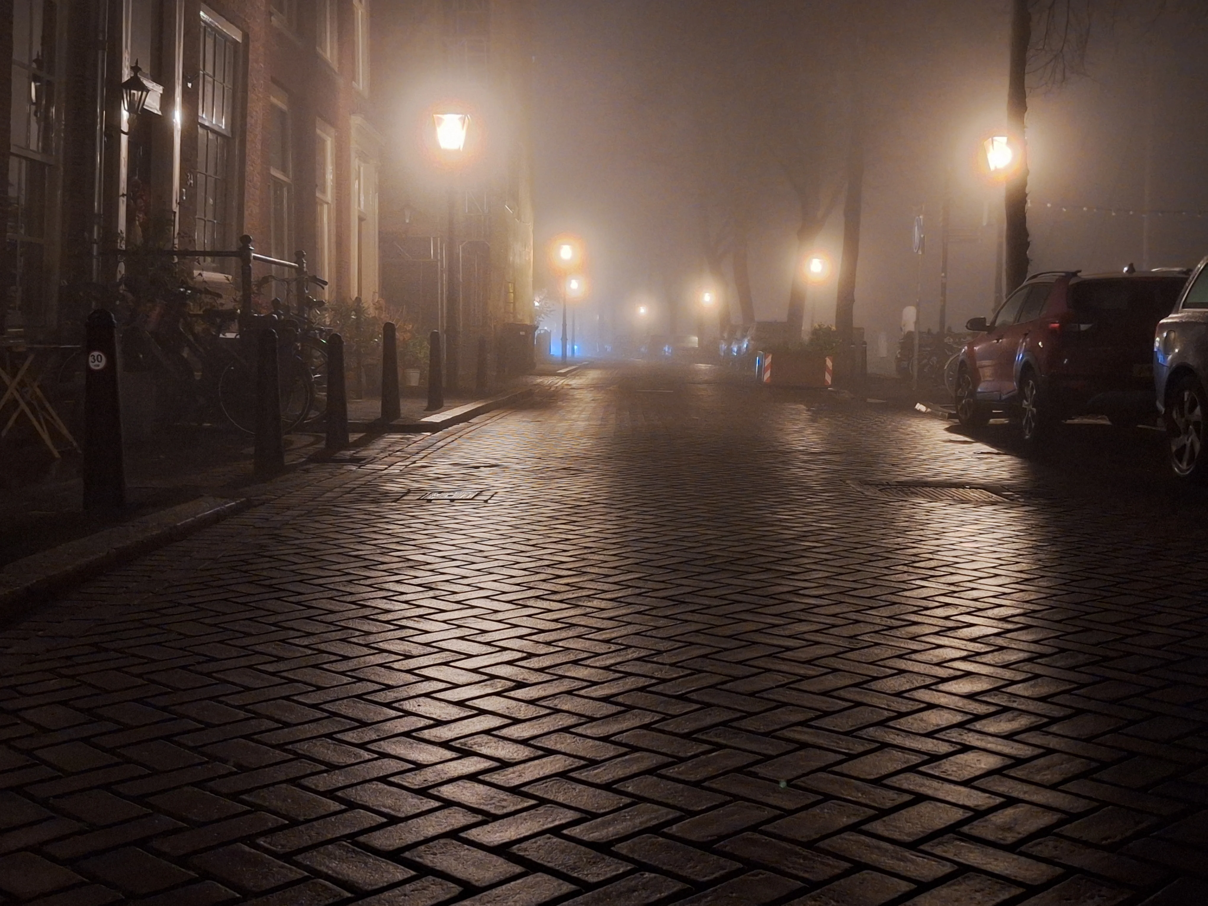 Wet cobbled street lit by lamps in fog
